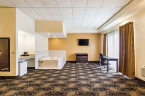 Habitación de hotel con bañera, escritorio, silla, televisor y alfombra estampada.