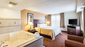 Une chambre d’hôtel avec une grande baignoire, un lit avec deux oreillers, une télévision et un bureau avec une lampe.