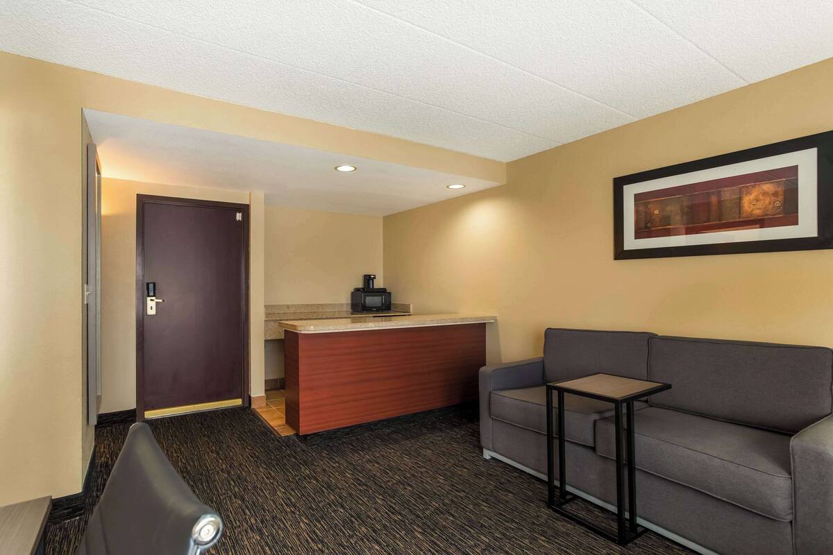 A hotel room with a reception desk, a gray sofa, a small table, and a framed picture on the wall.