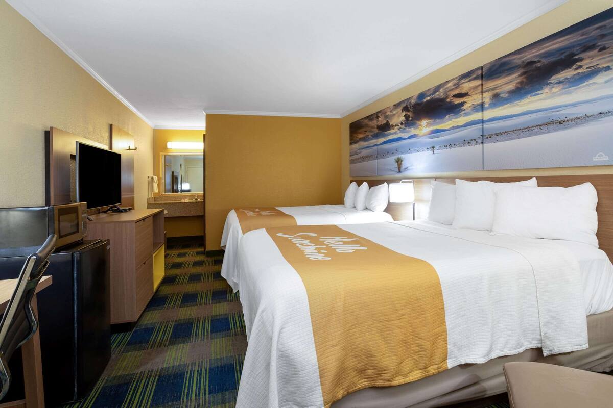 A hotel room with two beds, a TV, a desk, and a microwave.