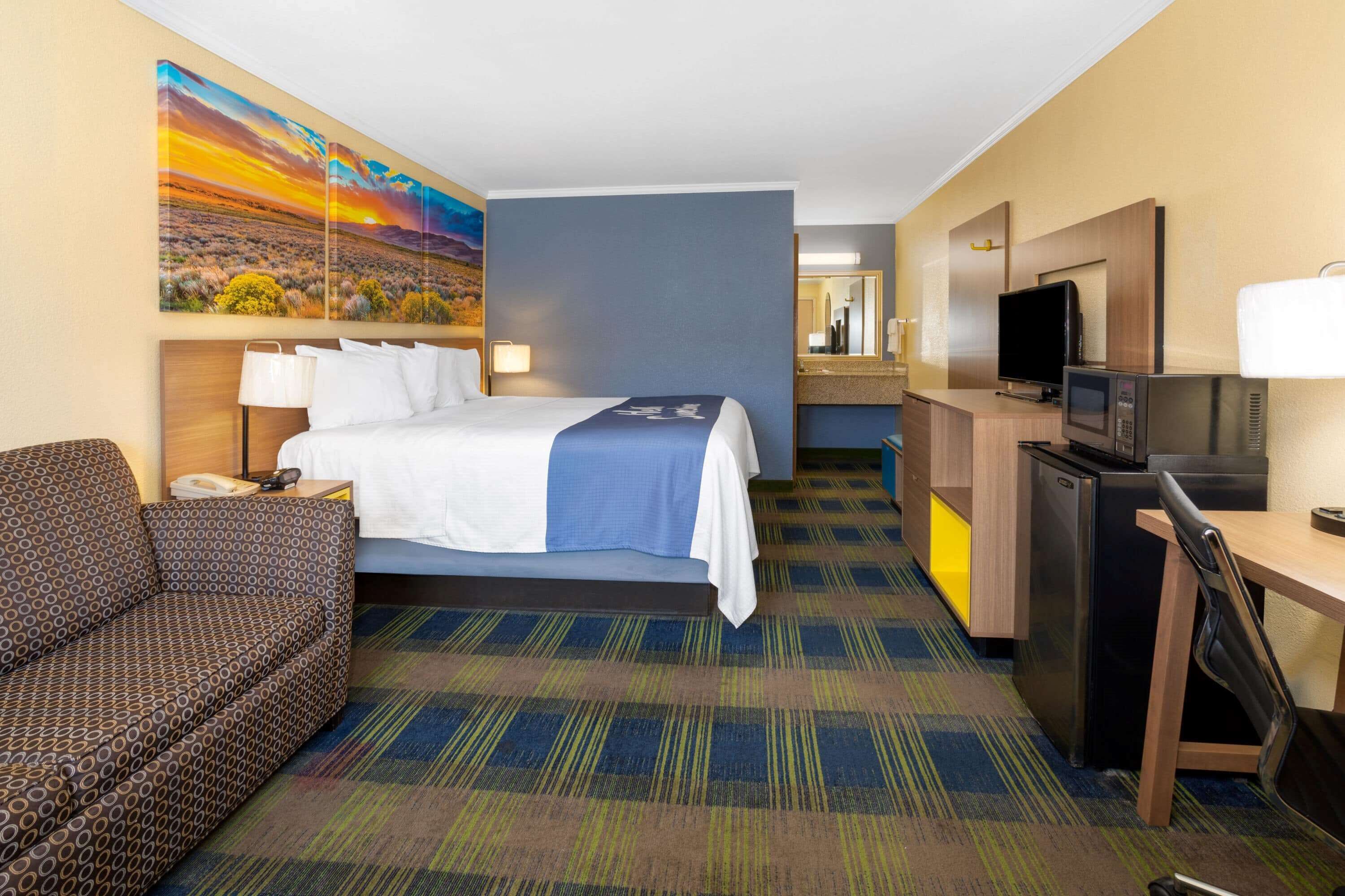 Habitación de hotel con cama, sofá, escritorio con televisor, microondas y refrigerador.