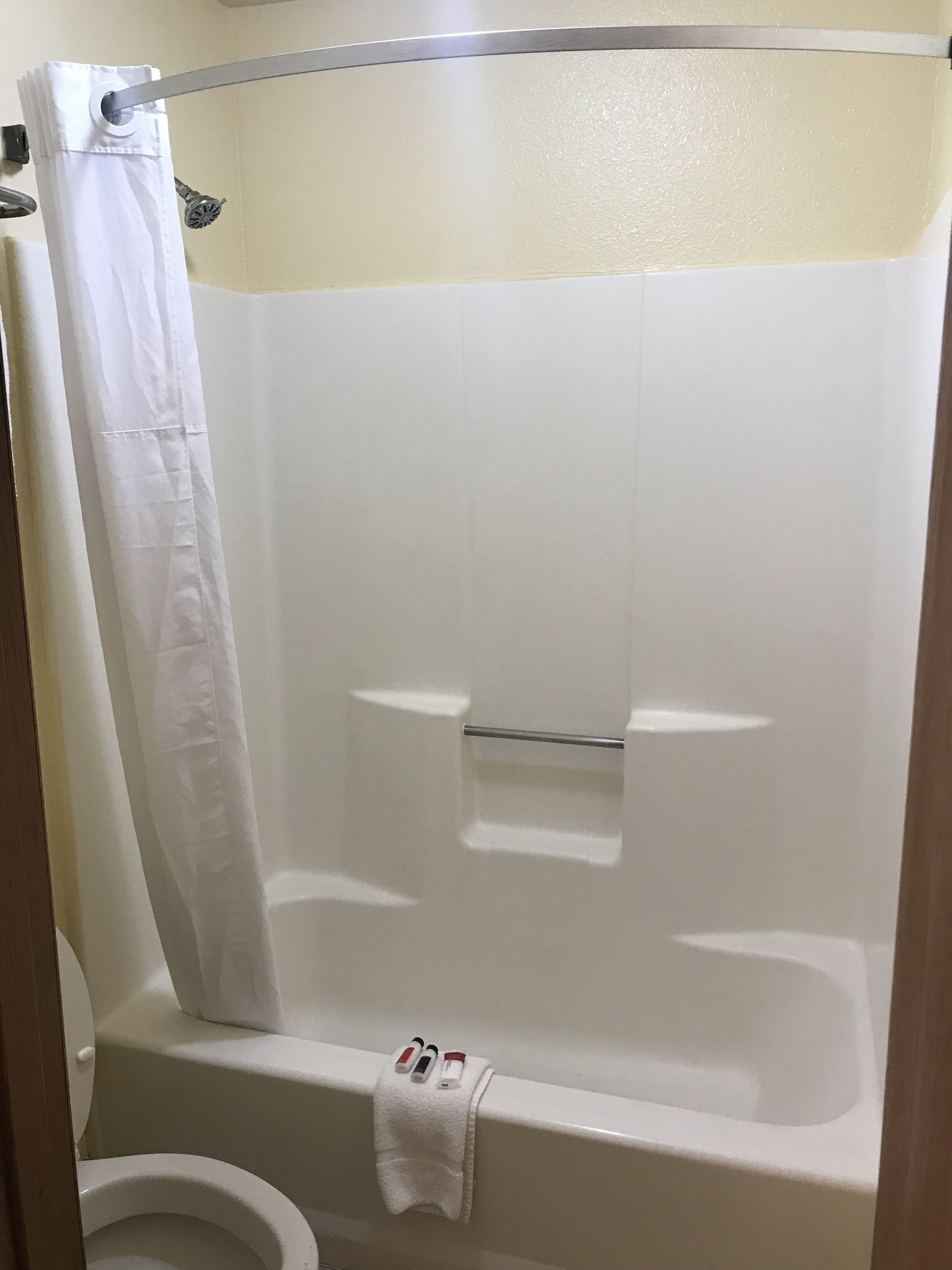 Een witte douche met gordijn, een handdoekrek en een toilet in de hoek.