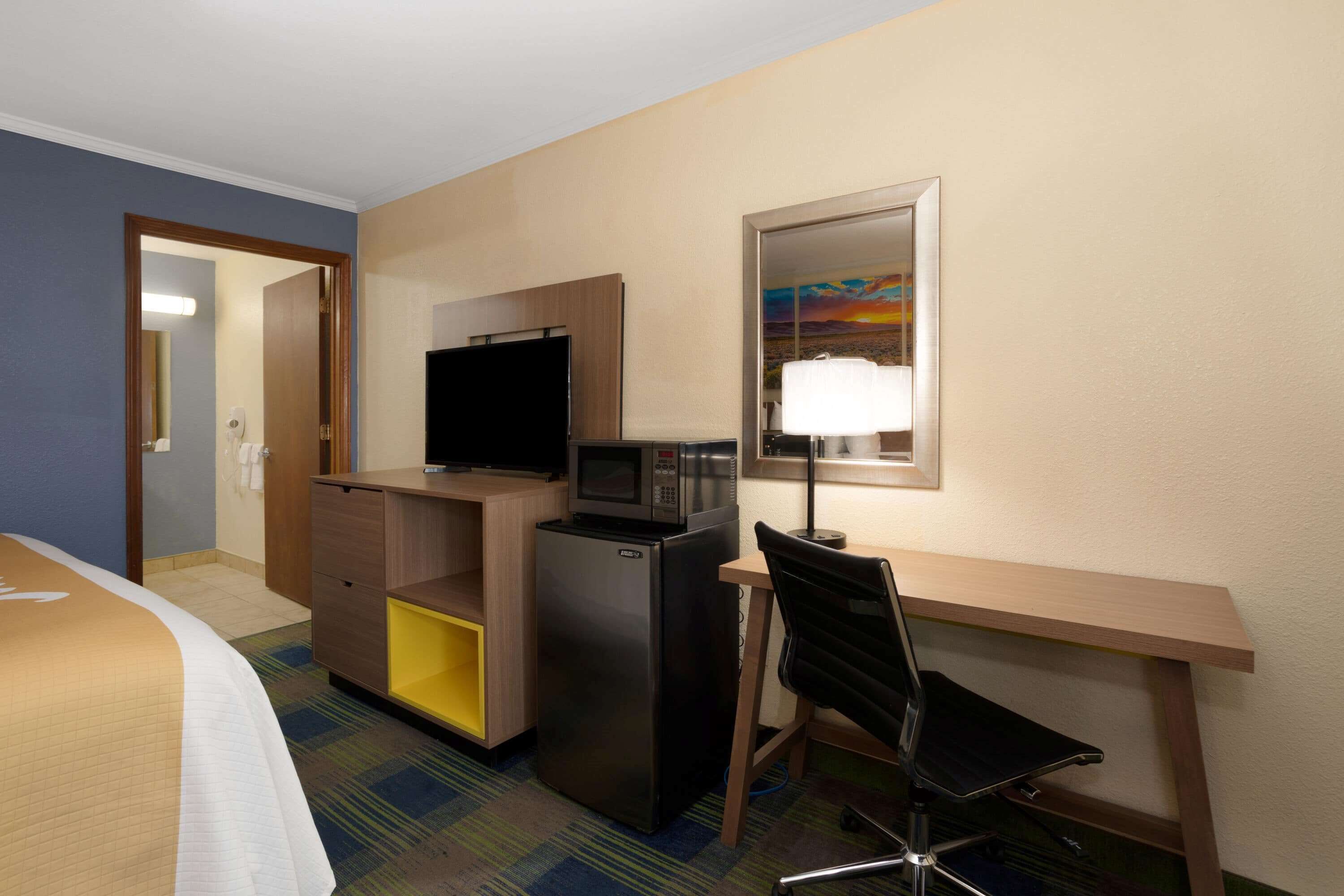 Habitación de hotel con una cama, un escritorio con computadora, un microondas, un refrigerador y un televisor.