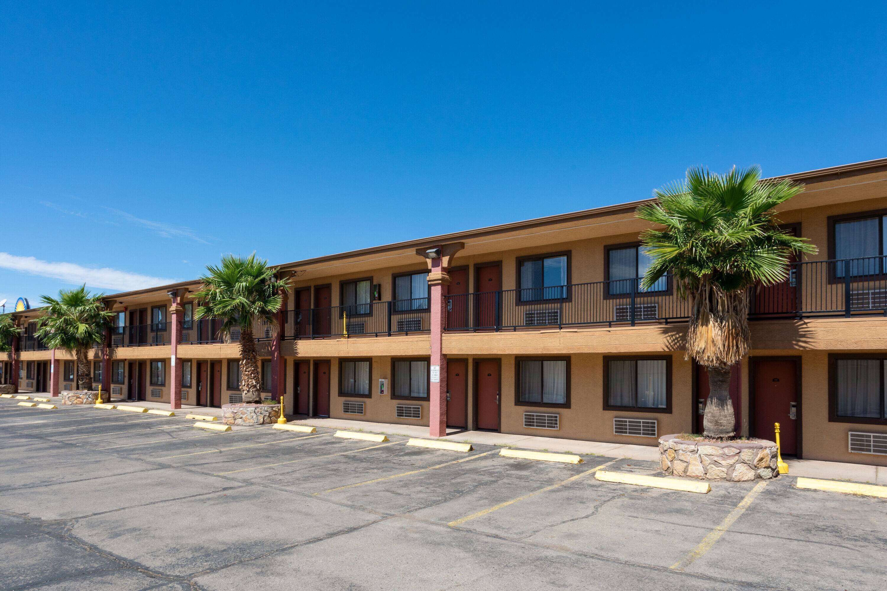 Un motel de varios pisos con una fila de habitaciones, cada una con un balcón y una palmera frente a ella.