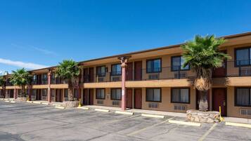 Un motel de varios pisos con una fila de habitaciones, cada una con un balcón y una palmera frente a ella.