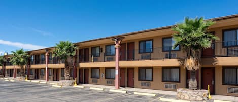 A multi-story motel with a row of rooms, each with a balcony and a palm tree in front.