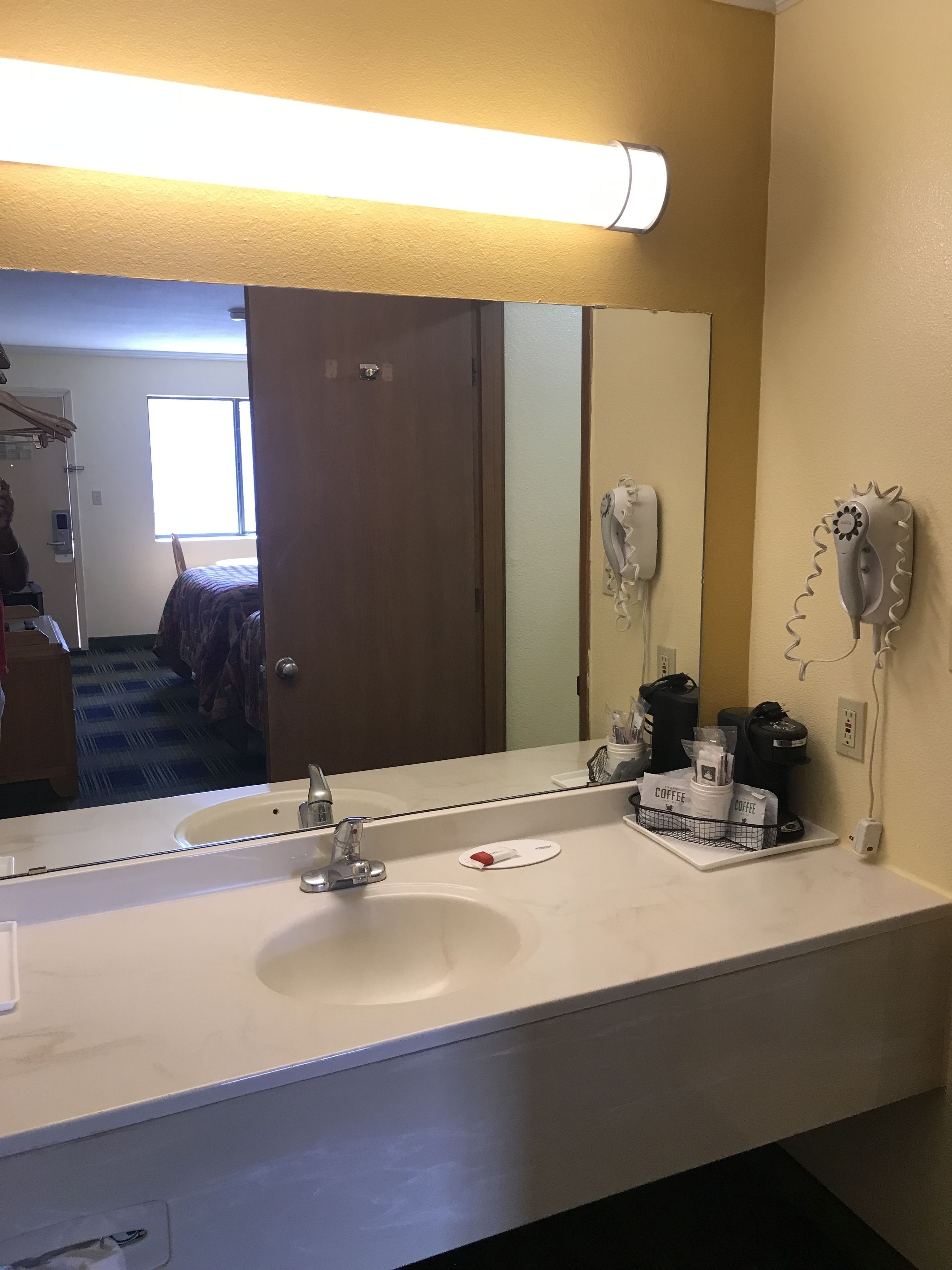 Un baño de hotel con un espejo grande, dos lavamanos, un secador de pelo y una estación de café.