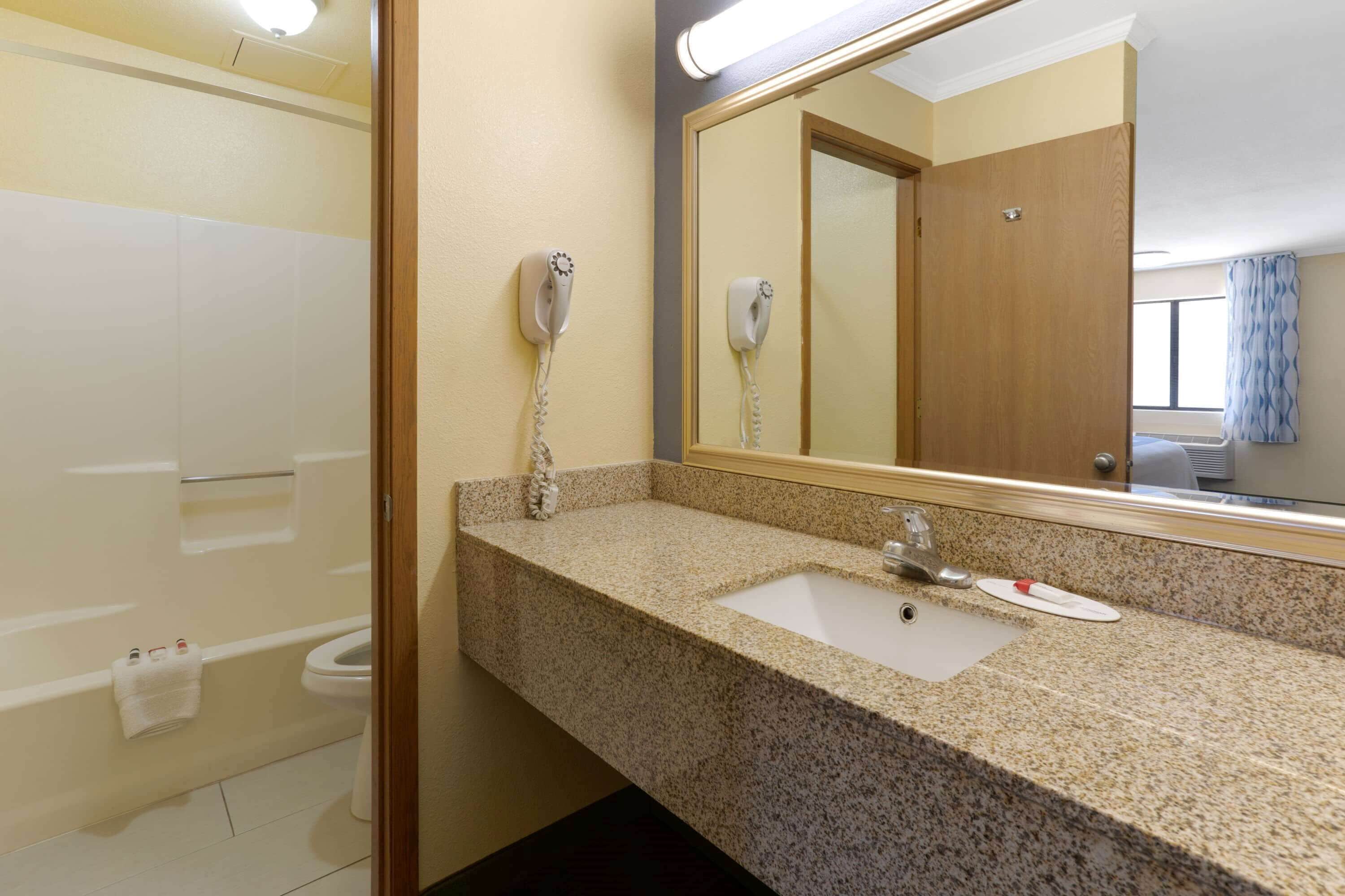 A bathroom with a granite countertop sink, a mirror, and a hairdryer mounted on the wall.