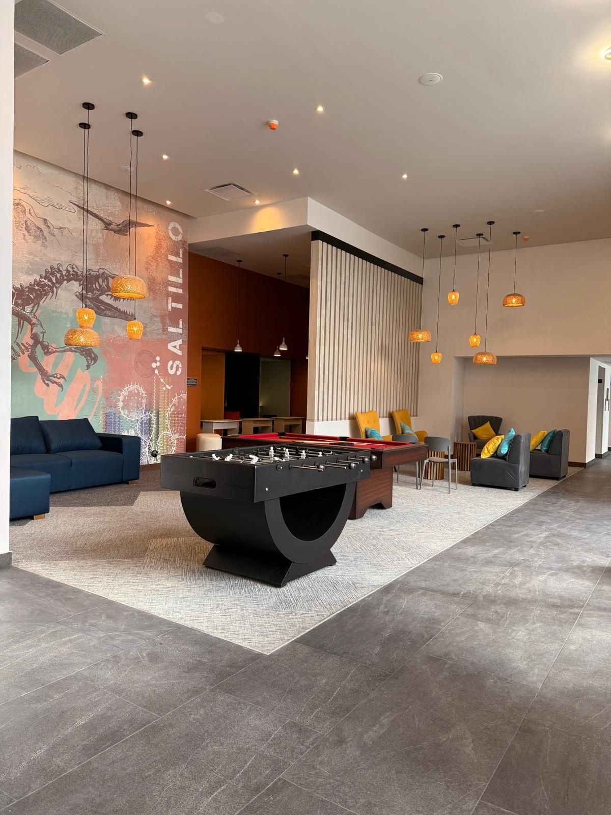 Una sala de estar moderna con mesa de futbolín, sofás y un mural en la pared.