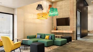 A modern living room with a sectional sofa, a yellow armchair, and a black ottoman. There are colorful pendant lights and a flat-screen TV mounted on the wall.