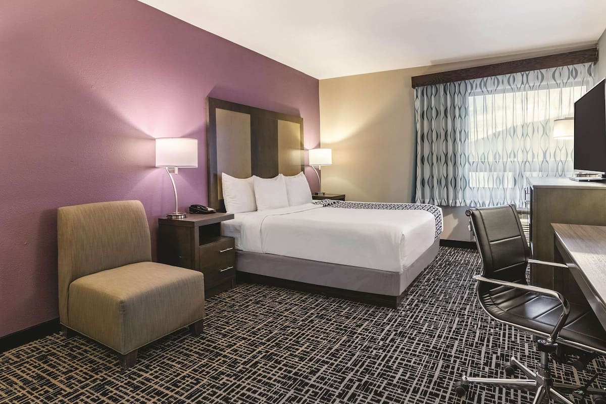 Une chambre d’hôtel comprenant un lit, des tables de chevet, une chaise, un bureau et un téléviseur.