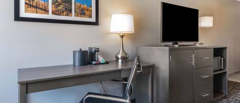 Een hotelkamer met een bureau, een stoel, een televisie, een lamp en een kast.