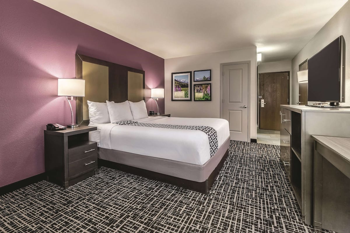 Une chambre d’hôtel avec un grand lit, des tables de chevet avec des lampes, une commode, un bureau avec un miroir et une porte donnant sur une salle de bain.