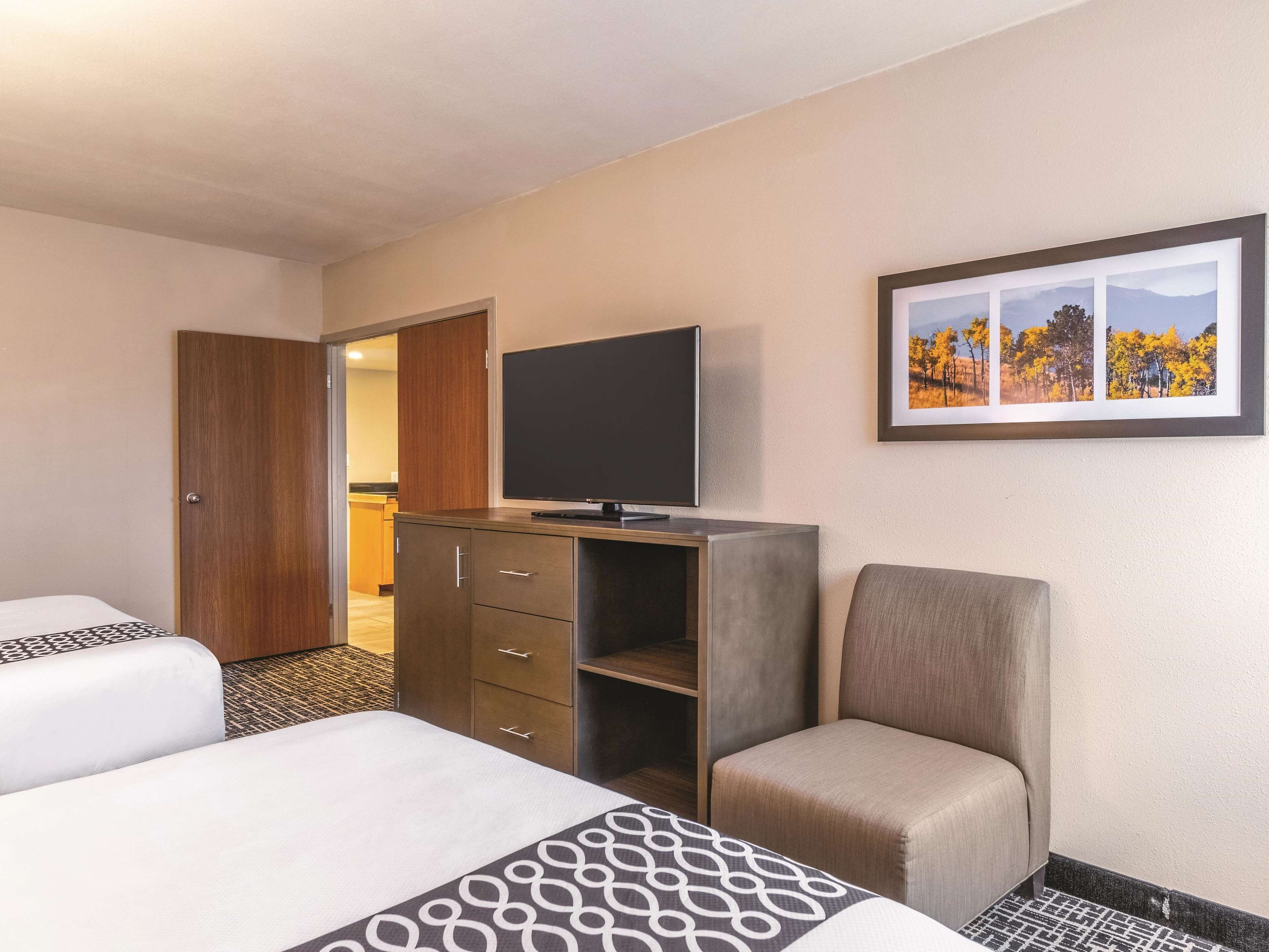 A hotel room with two beds, a TV on a cabinet, a chair, and a framed picture on the wall.