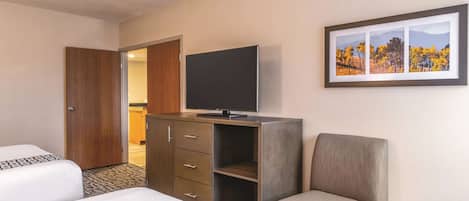 A hotel room with two beds, a TV on a cabinet, a chair, and a framed picture on the wall.