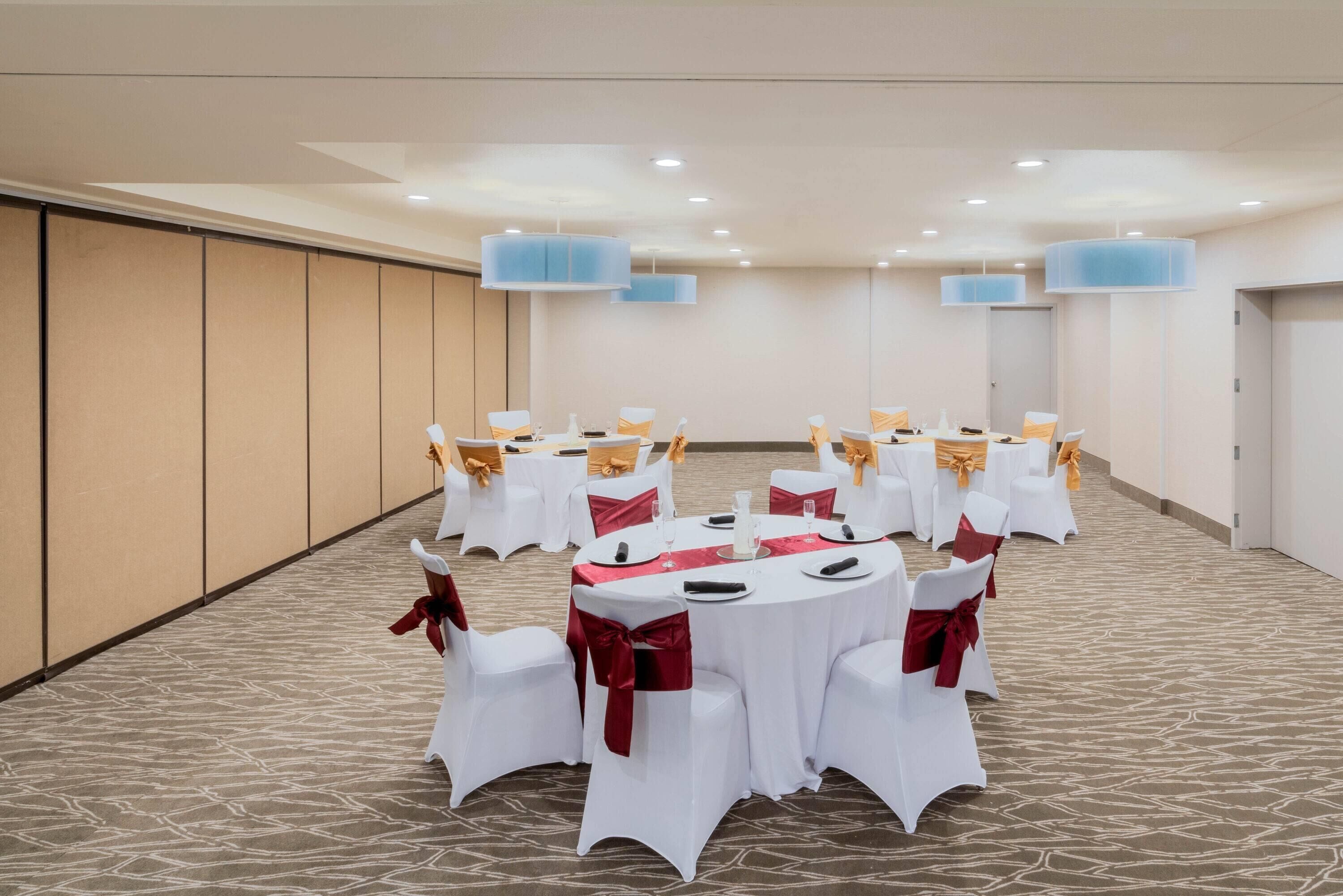 A conference room with round tables, white chairs with red sashes, and blue pendant lights.