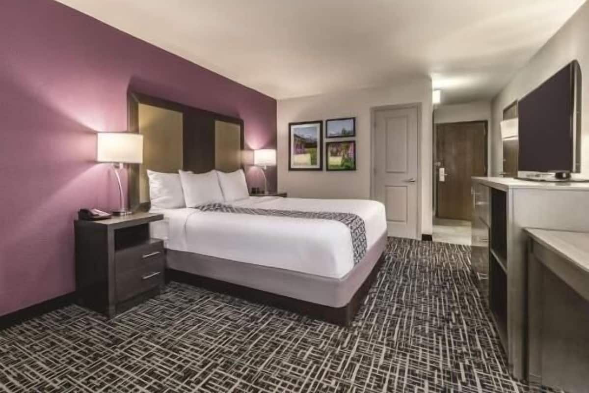 Une chambre d’hôtel comprenant un lit, des tables de chevet, un bureau, une chaise, un miroir et une porte.