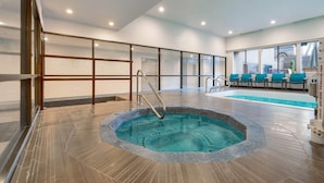 Una piscina interior moderna con un elemento acuático cristalino, rodeada de suelo de baldosas y barandillas de vidrio.
