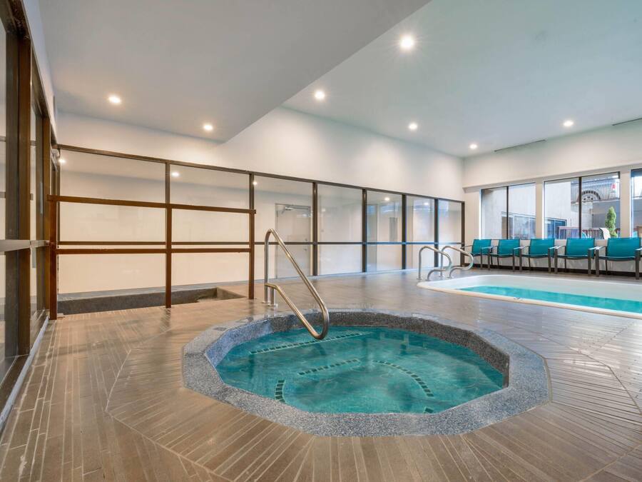 A modern indoor swimming pool with a clear water feature, surrounded by a tiled floor and glass railings.