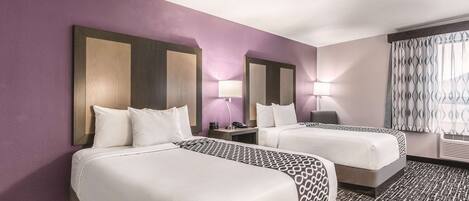 Habitación de hotel con dos camas, un espejo grande, lámparas de noche y una ventana con cortinas.