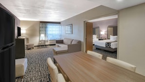 Habitación de hotel con una cama grande, un sofá, una mesa de comedor y un televisor.