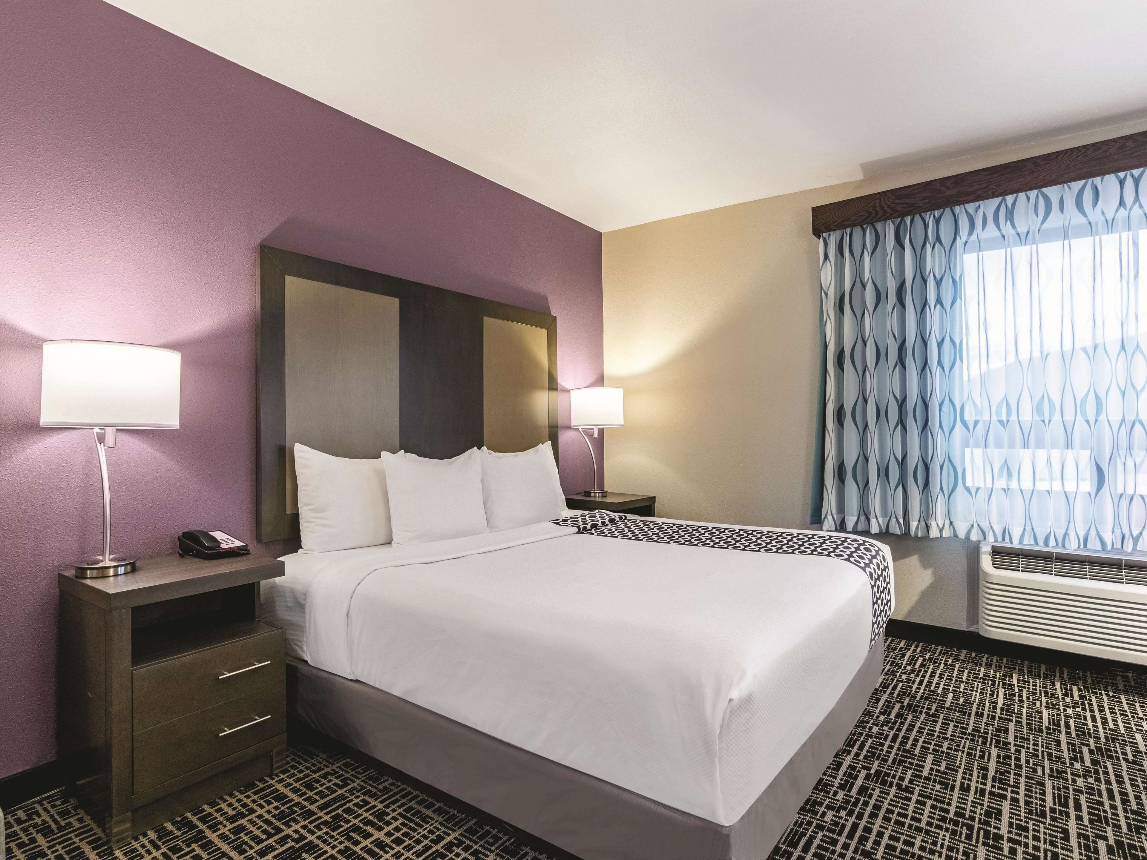 A hotel room with a large bed, two bedside tables, a telephone, and a window with patterned curtains.
