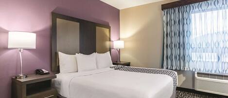 A hotel room with a large bed, two bedside tables, a telephone, and a window with patterned curtains.