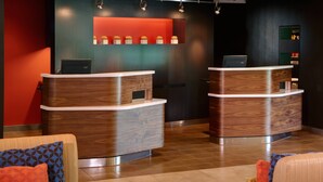 A reception area with two wooden reception desks, a red accent wall, and a seating area with patterned cushions. - Courtyard by Marriott Lexington North (Lexington)