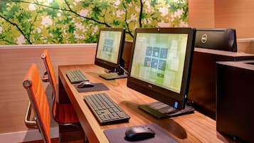 Una hilera de escritorios con computadoras, teclados y ratones, frente a una pared con un mural de hojas.