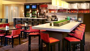 A bar area with multiple stools and tables, a television screen, and a variety of bottles and glasses on shelves. - Courtyard by Marriott Lexington North (Lexington)
