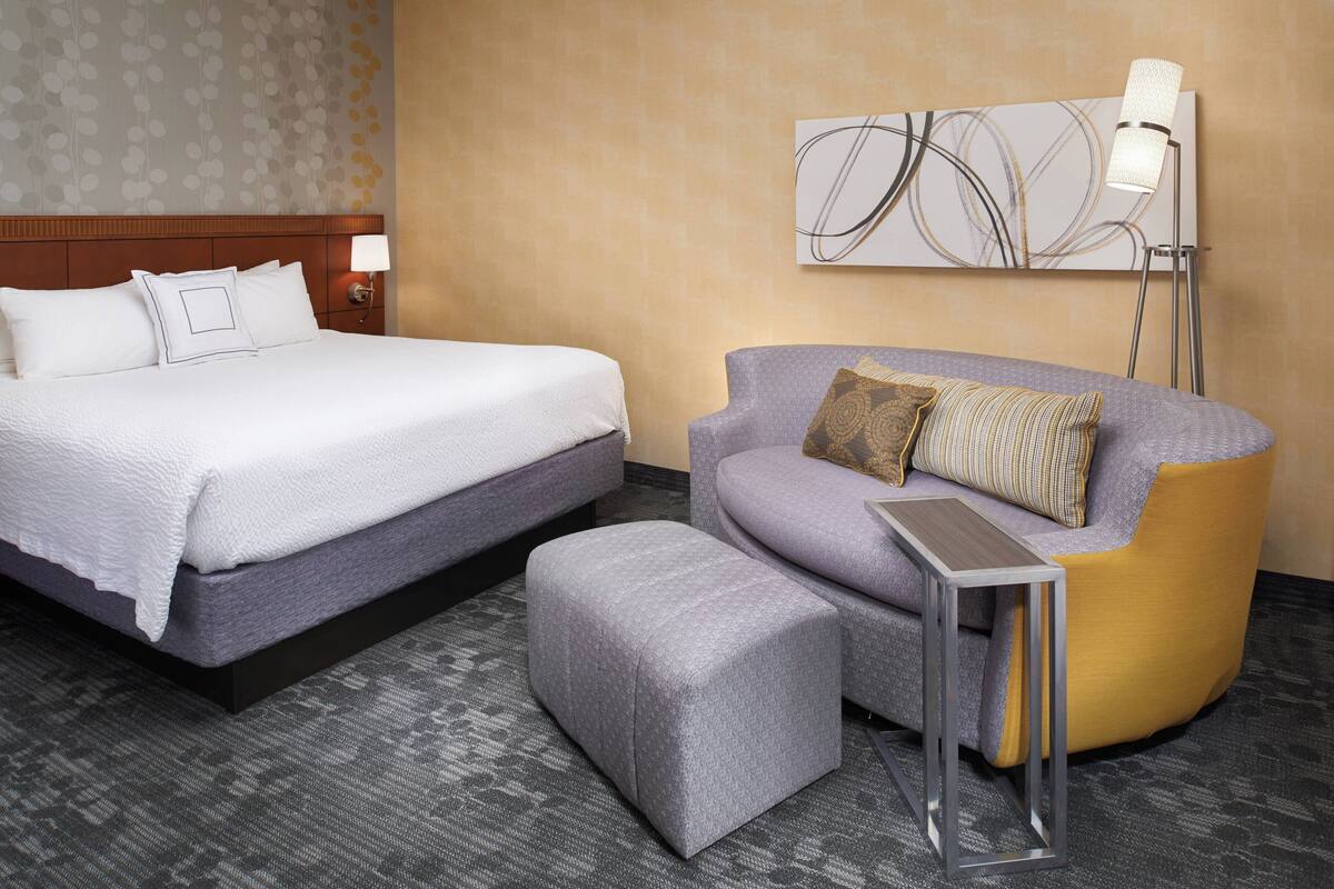 Ein Hotelzimmer mit Bett, Sofa, kleinem Tisch und Stehlampe.