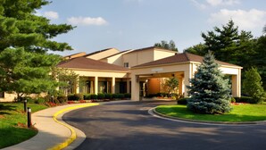 A hotel with a curved driveway, covered parking, and a well-maintained lawn with trees and shrubs. - Courtyard by Marriott Lexington North (Lexington)