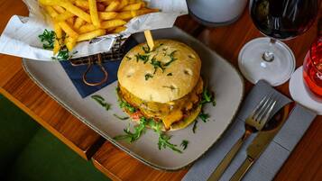 A meal with a burger and fries on a plate, a glass of red wine, and a napkin with cutlery on a wooden table.