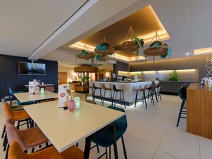A modern restaurant with a bar area, multiple seating options, and a large TV screen. - Novotel Nuernberg Messezentrum (Nuremberg)