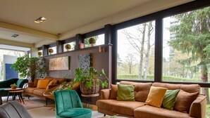 A modern living room with a sofa, chairs, a coffee table, and large windows with a view of trees. - Novotel Nuernberg Messezentrum (Nuremberg)