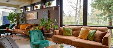 Un salon moderne avec un canapé, des fauteuils, une table basse et de grandes fenêtres donnant sur la verdure.