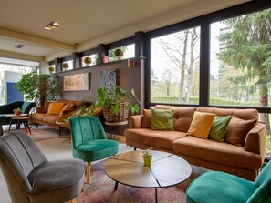 A modern living room with a sofa, chairs, a coffee table, and large windows with a view of trees. - Novotel Nuernberg Messezentrum (Nuremberg)
