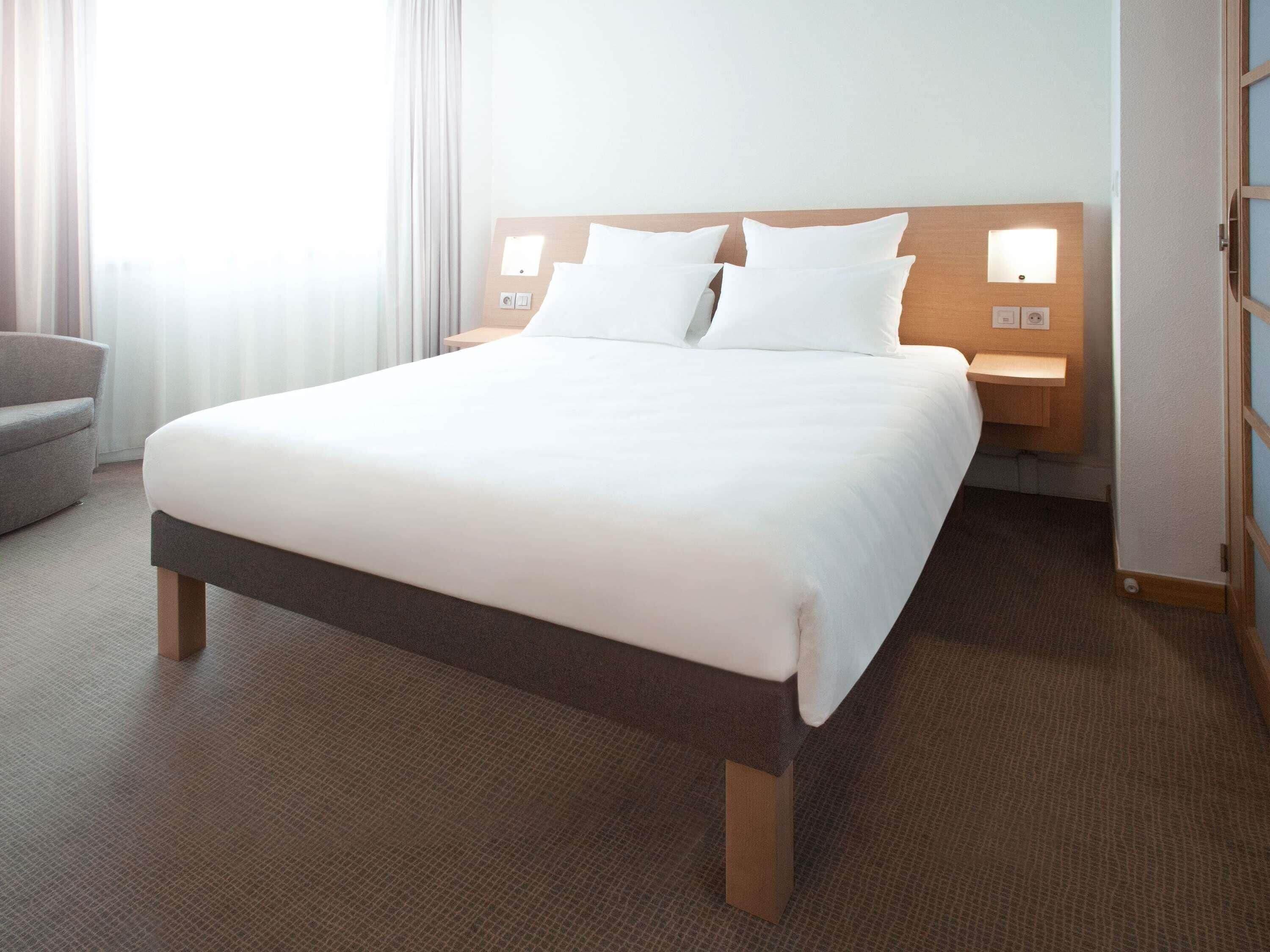 A hotel room with a large bed, two bedside tables, a chair, and a window with curtains.