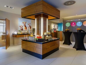 A modern reception area with a wooden reception desk, a large painting of deer, and a wall with circular signs indicating amenities like 'Health & Beauty Food' and 'Comfort Food'. - Novotel Nuernberg Messezentrum (Nuremberg)