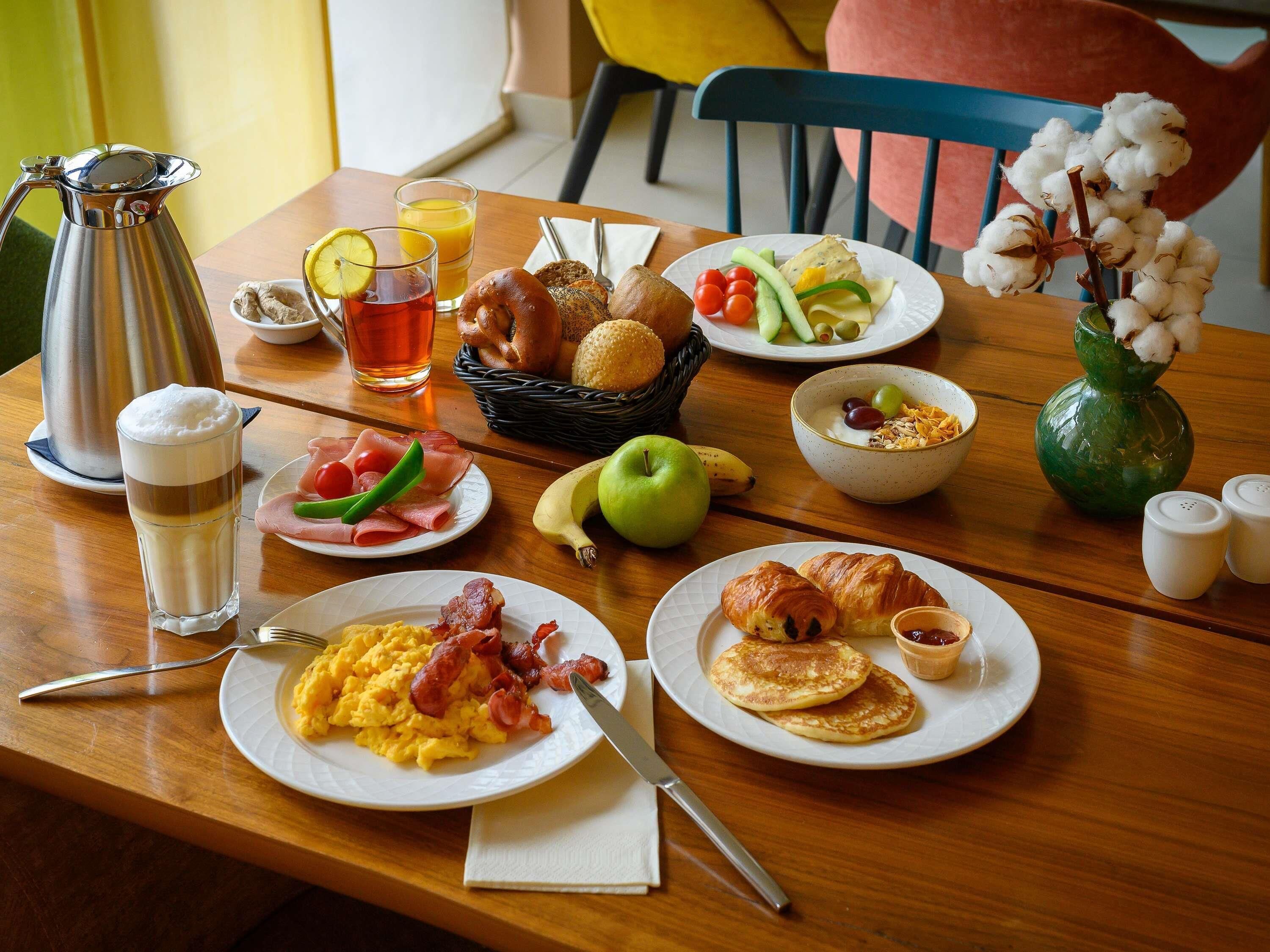 A breakfast table with various food items, a coffee pot, and a vase with cotton plants.