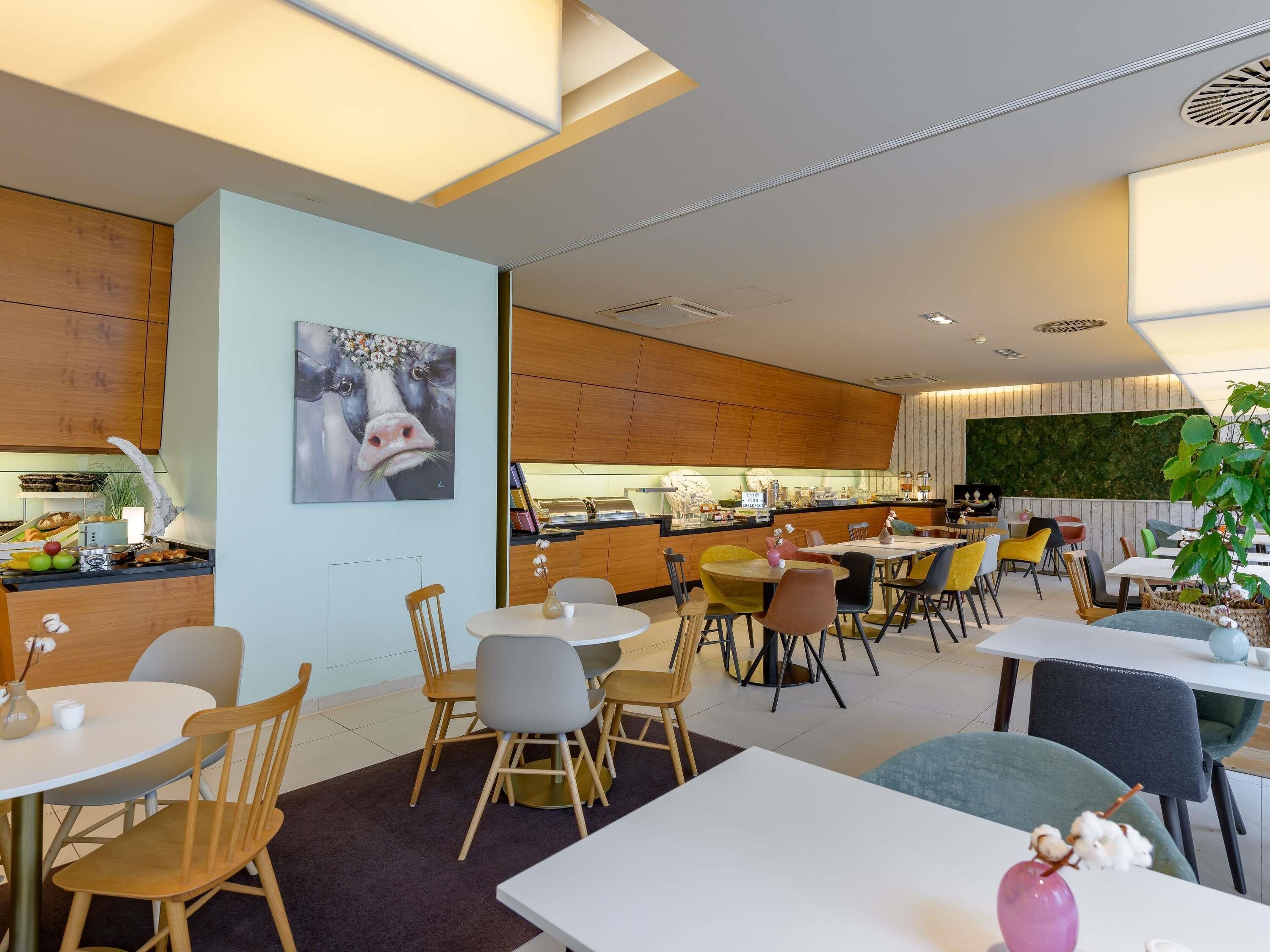 A modern restaurant with wooden paneling, a central bar area, and various seating options including round tables and chairs.