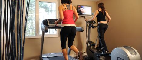 Two people using treadmills in a room with a TV and windows.