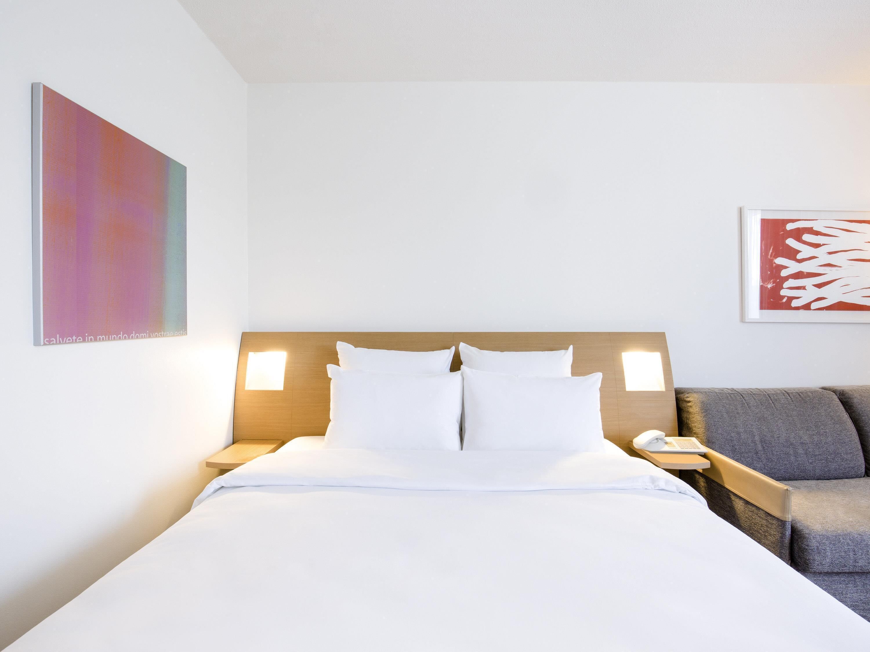 A hotel room with a bed, two bedside tables, a chair, and artwork on the walls.