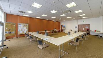 Ein Konferenzraum mit langem Tisch, Stühlen, einer Tafel und einer Projektionsleinwand.