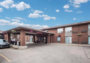 A hotel entrance with a covered area, brick facade, and a parking lot.