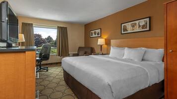 Een hotelkamer met een groot bed, een bureau met een computer, een stoel en een raam met gordijnen.