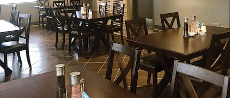 Un comedor con varias mesas y sillas, un extintor y saleros y pimenteros sobre las mesas.
