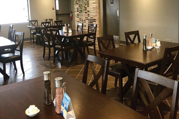 A dining area with multiple tables and chairs, a fire extinguisher, and salt and pepper shakers on the tables. - Comfort Inn West Edmonton (Edmonton)