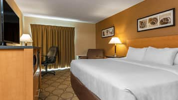 Habitación de hotel con una cama grande, un escritorio con televisor, una silla, una lámpara de escritorio y una ventana con cortinas.