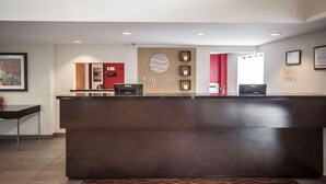Un comptoir d’accueil d’hôtel avec une enseigne indiquant « Comfort Inn ». On peut voir deux écrans d’ordinateur sur le comptoir, et une porte rouge est visible à l’arrière-plan.
